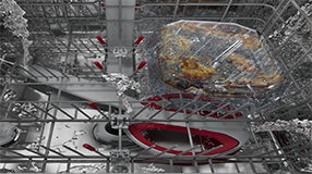 Innenraum einer Spülmaschine während des Spülvorgangs, Wasserstrahlen reinigen eingebrannte Speisereste aus einer Auflaufform im oberen Korb