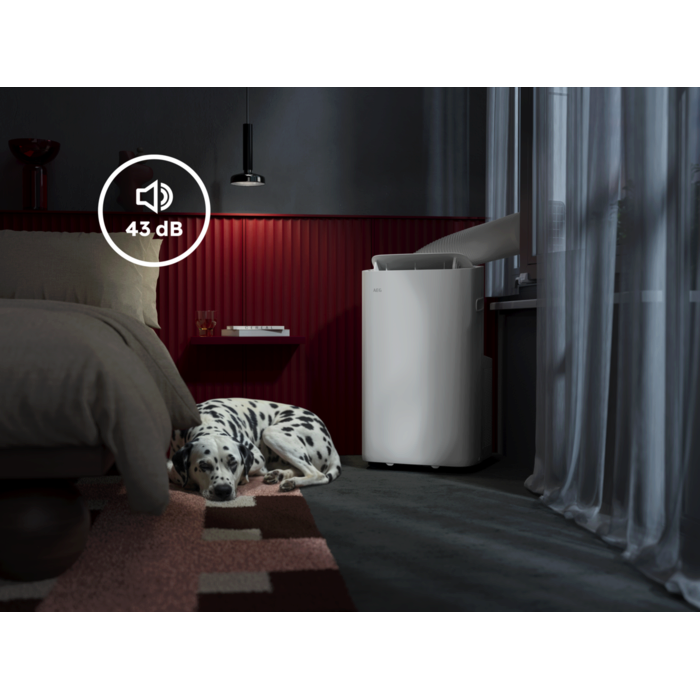 Leiser mobiler Klimagerät (43 dB) in einem modernen Schlafzimmer, neben einem Bett liegt ein schlafender Dalmatiner; das Gerät steht am Fenster mit Abluftschlauch.