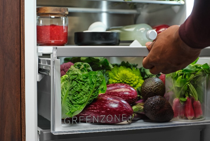 Mann zieht eine mit Gemüse gefüllte Greenzone-Schublade im Kühlschrank heraus.