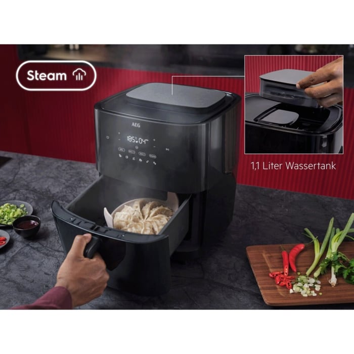 Airfryer mit Dampffunktion; Person zieht Schublade mit gedämpften Teigtaschen heraus. Links Steam‑Symbol, rechts Wassertank‑Hinweis