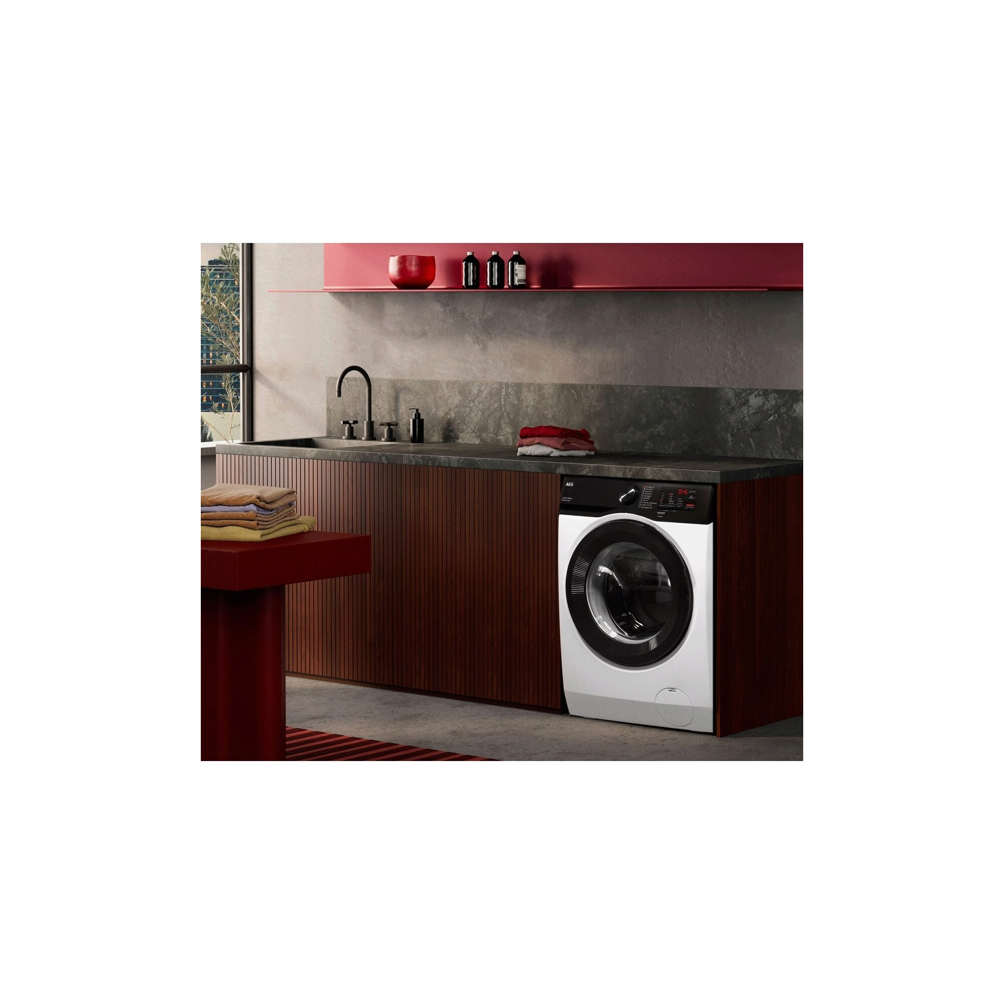 „AEG-Waschmaschine integriert in dunkle Holzfront mit grauer Arbeitsplatte und roten Akzenten.“