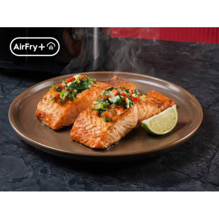 Gebratene Lachsfilets mit Gemüse-Topping auf Teller, daneben Limettenstück; links AirFry‑Plus‑Symbol
