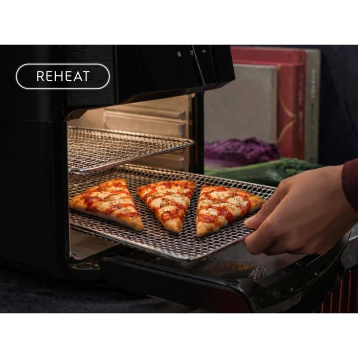 Hand schiebt ein Blech mit drei Pizzastücken in einen Airfryer; links oben Reheat‑Symbol
