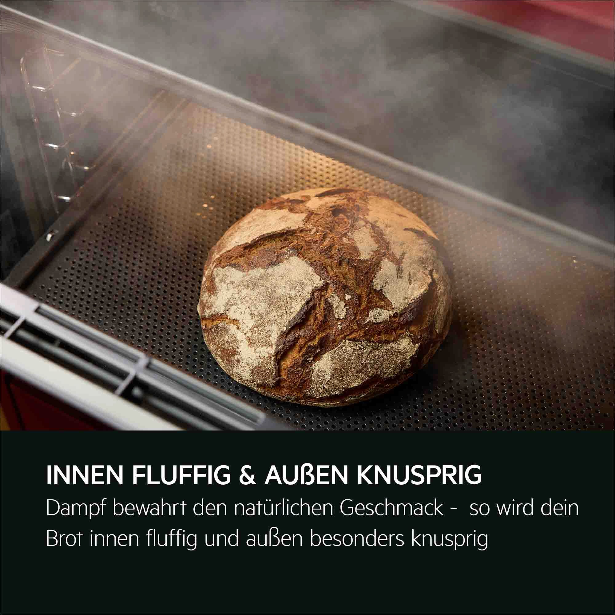 Rundes Brot mit dunkler Kruste liegt auf Backblech im Ofen, Dampf steigt auf.