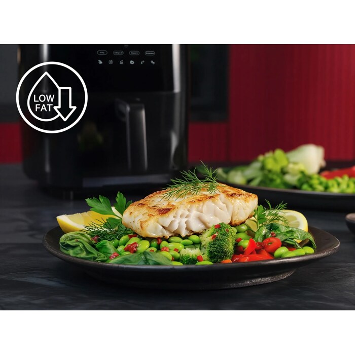 Gebratenes Fischfilet auf Gemüseplatte; links oben Low‑Fat‑Symbol. Im Hintergrund steht ein Airfryer