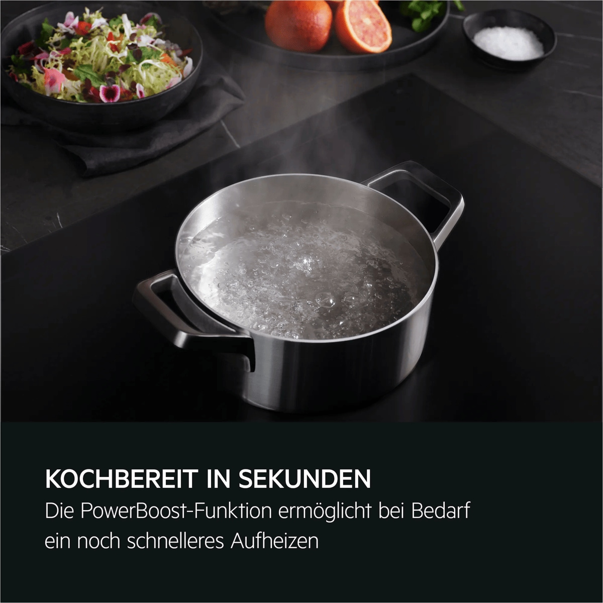 Ein Topf mit kochendem Wasser steht auf einem Induktionskochfeld, im Hintergrund liegen Obst und eine Salatschale.
