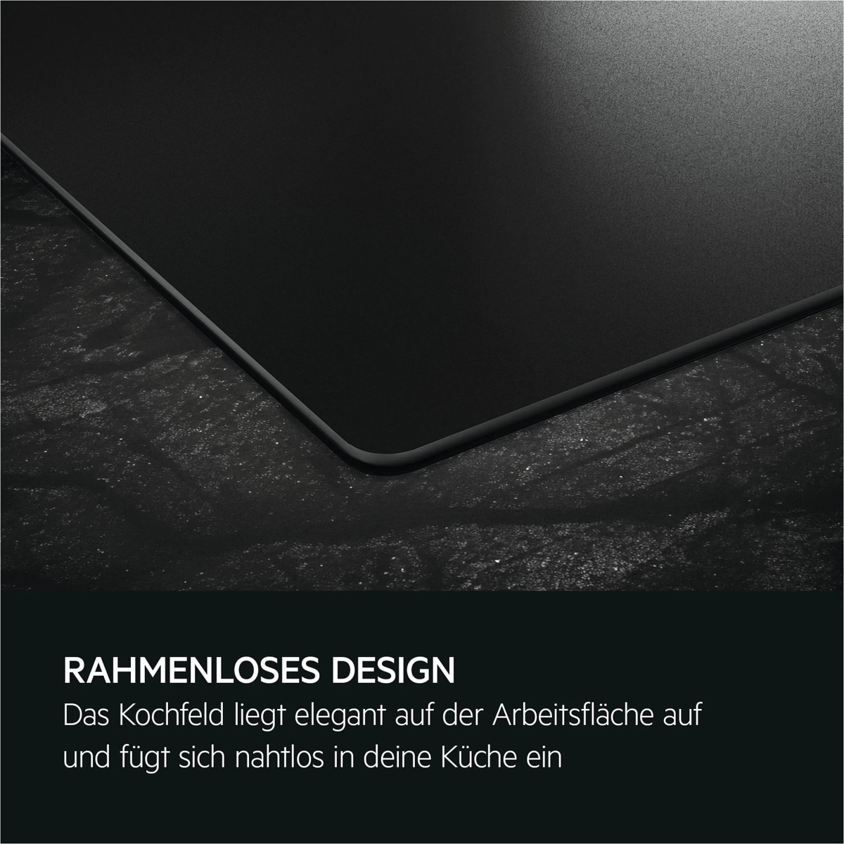 Die Ecke eines rahmenlosen schwarzen Kochfelds liegt flach und bündig auf einer dunklen Arbeitsplatte.