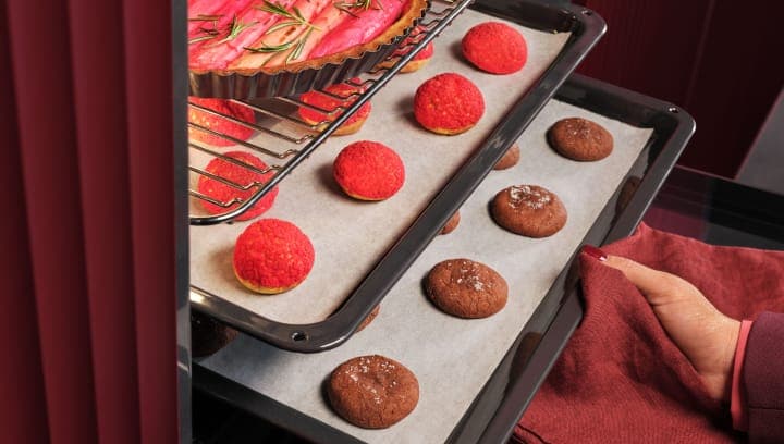 Eine Person nimmt ein Backblech mit Gebäck aus einem Backofen.