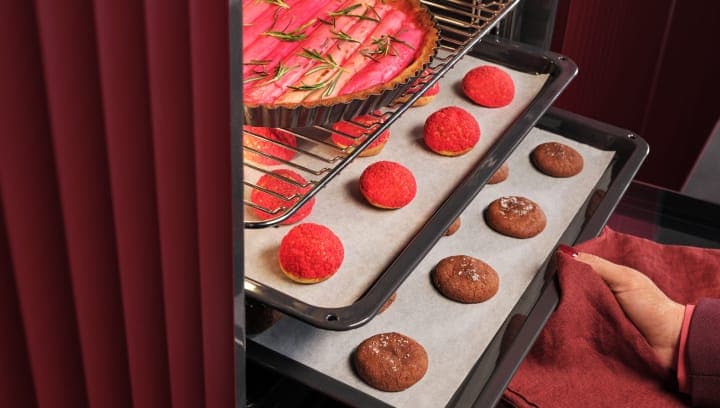 Eine Person nimmt ein Backblech mit Gebäck aus einem Backofen.
