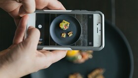 Jemand, der ein Foto von einem Teller mit einer perfekt präsentiertem Gourmet-Speise macht