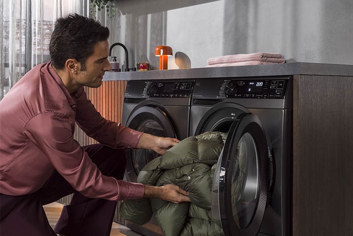 Mann l&auml;dt Daunenjacke in AEG Waschmaschine mit gro&szlig;er Trommelkapazit&auml;t in modernem Hauswirtschaftsraum