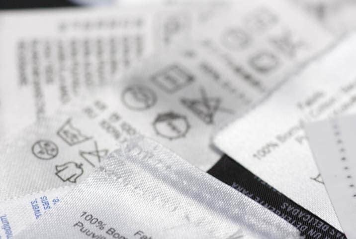 Nahaufnahme von Pflegeetiketten auf Kleidungsst&uuml;cken mit W&auml;schepflegesymbolen und Materialangaben