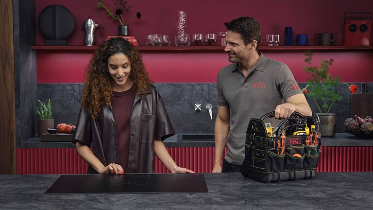 Eine Kundin und ein Service-Techniker stehen in einer roten Küche mit Induktionskochfeld.