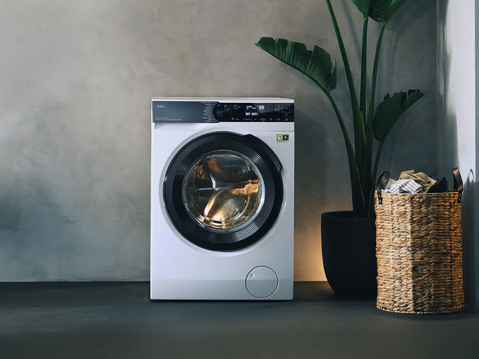 AEG Serie 9000 Waschmaschine freistehend neben Wäschekorb und Zimmerpflanze