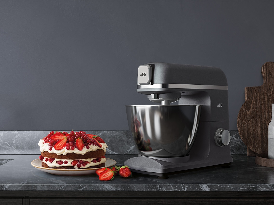 AEG K&uuml;chenmaschine in Grau mit Edelstahlsch&uuml;ssel neben Beerenkuchen mit Erdbeeren und Johannisbeeren auf Marmorarbeitsfl&auml;che