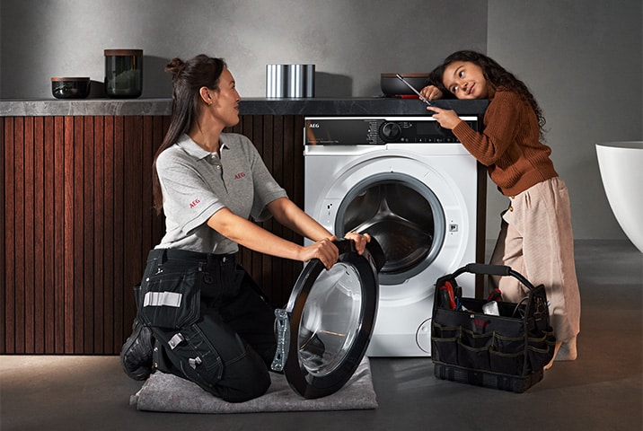 AEG Servicetechnikerin tauscht T&uuml;rdichtung an AEG Waschmaschine aus, ein junges M&auml;dchen schaut interessiert zu