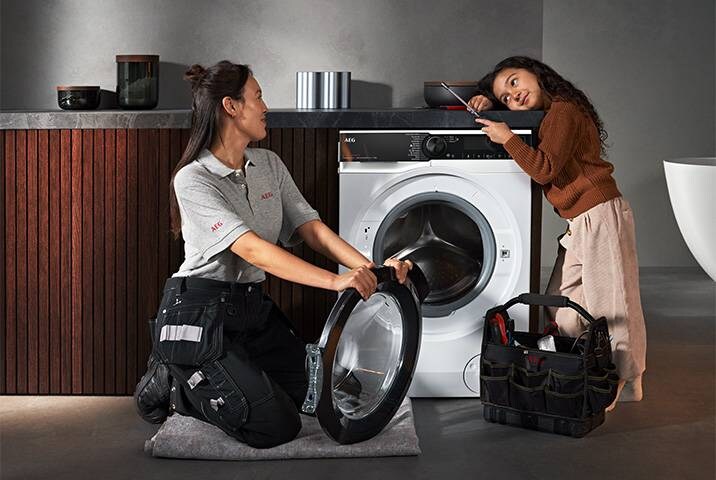 AEG Servicetechnikerin tauscht Türdichtung an AEG Waschmaschine aus, ein junges Mädchen schaut interessiert zu