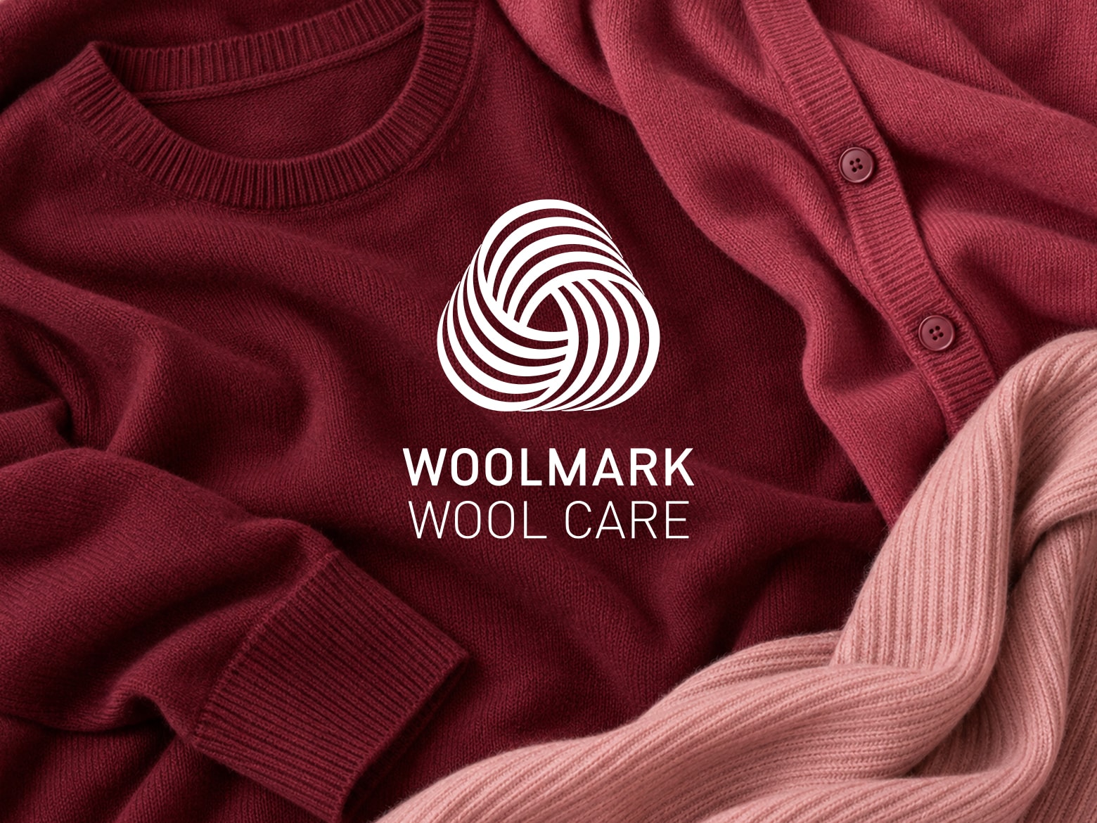 Woolmark Label, im Hintergrund befinden sich mehrere Wollpullover in Rottönen
