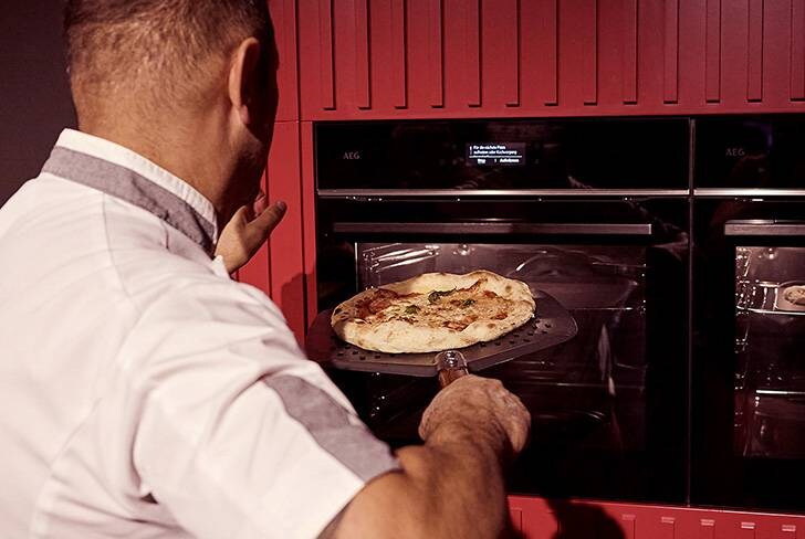 Ein Mann schiebt eine Pizza in einen AEG Backofen