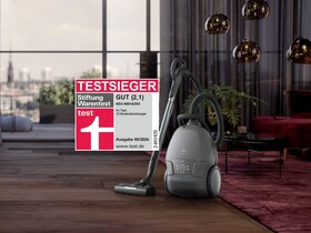 Der AEG ANIMAL 8000 Bodenstaubsauger AB81A2DG steht in einem Wohnraum, daneben ein Logo der Stiftung Warentest