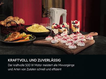 Tisch mit Speisen und weißem Handmixer vor rotem Hintergrund.