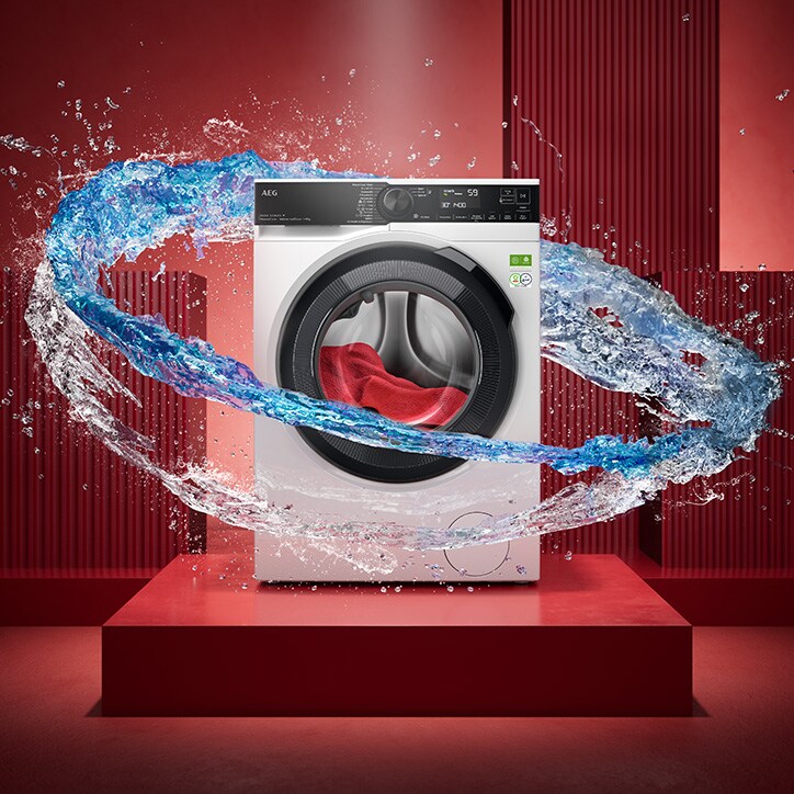 AEG‑Frontlader‑Waschmaschine auf rotem Podest, umgeben von einem dynamischen Wasserwirbel, der die Trommel umkreist und effektive Fleckenentfernung symbolisiert.